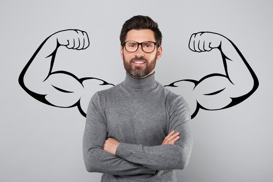 Handsome man with drawing of strong arms behind him on grey background