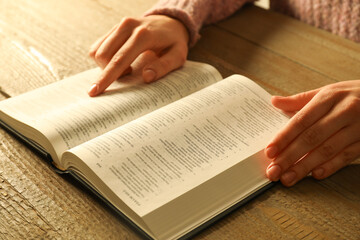 Naklejka premium Woman reading Holy Bible in English language at wooden table, closeup