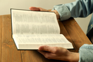 Woman reading Holy Bible in English language at wooden table, closeup