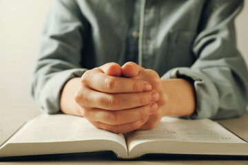 Woman with open Holy Bible in English language praying at beige table, closeup