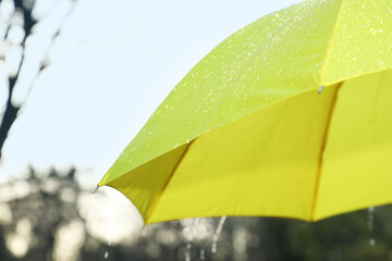 Open yellow umbrella under pouring rain outdoors, closeup. Space for text
