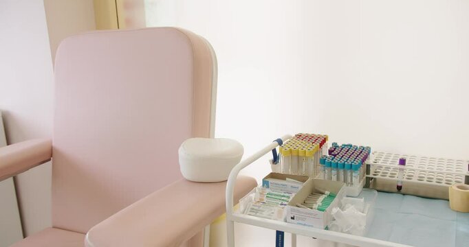 An equipped medical laboratory with a pink chair beside a table holding blood test tubes, syringes, and other medical supplies. Modern Medical Clinic with Blood Test Equipment and Chair