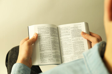 Man reading Holy Bible in English language on light background, closeup