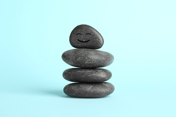 Stack of rocks with drawn smiley face on light blue background. Harmony and life balance