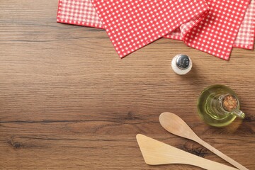 Checkered tablecloth, cooking utensils, oil and salt on wooden table, flat lay. Space for text