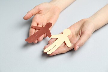 Stop racism. Woman holding human paper figures of different colors on light grey background, closeup