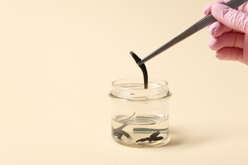 Woman taking medicinal leech from jar with tweezers on pale yellow background, closeup