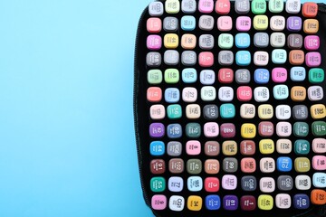 Many colorful markers in bag on light blue background, top view. Space for text