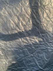 Fototapeta premium Sunlight casts intricate shadow patterns on a crumpled metallic surface in the late afternoon, highlighting textures and shapes that evoke curiosity
