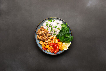 Fresh vegan bowl with cherry tomatoes, tofu, white rice, spinach leaves, fried mushrooms and green pea on black stone background top view. Healthy diet food concept. 