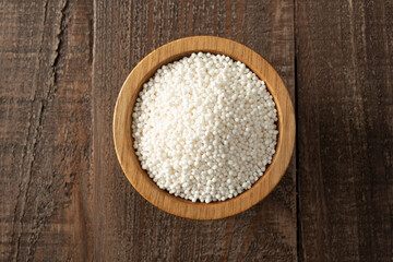 A top down view of dry tapioca pearls, in a wood bowl. 