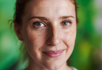 Extreme close-up portrait of a woman with freckles, smiling gently, with a blurry green background.