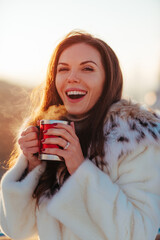 Young beautiful woman holding cup with hot drink, winter portrait on sunny day