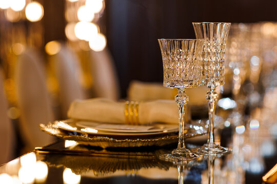 Luxury table setting with plates, napkin with ring, crystal wineglasses and golden cutlery on mirror table for romantic dinner in restaurant, bokeh. Christmas, New Year 2026 dinner. Wedding, birthday