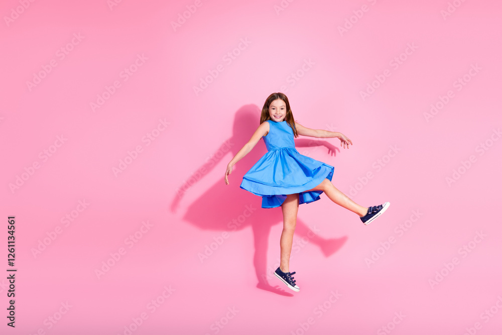 Wall mural Playful young girl in a stylish blue dress poses joyfully on a vibrant pink background