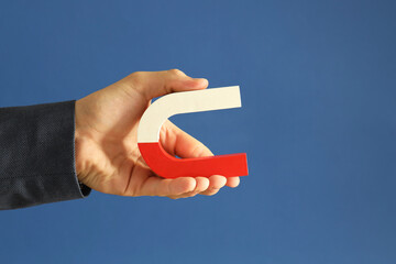 Man holding horseshoe magnet on blue background, closeup. Space for text