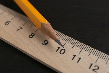 Ruler and pencil on black wooden table, closeup