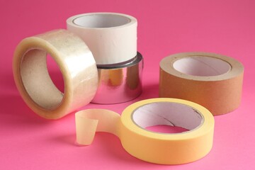 Rolls of different adhesive tapes on pink background, closeup