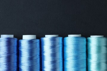 Spools of colorful sewing threads on black background, flat lay