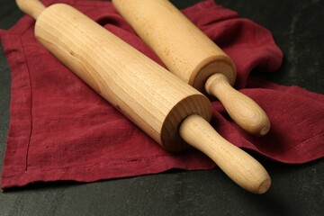 Wooden rolling pins and napkin on dark gray textured table, closeup