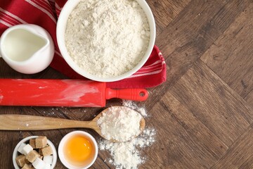 Rolling pin and ingredients for dough on wooden table, flat lay. Space for text