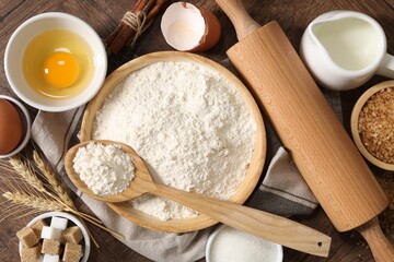 Rolling pin and ingredients for dough on wooden table, flat lay