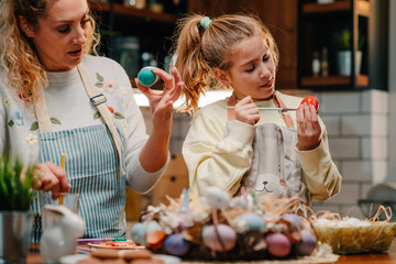 Mother and daughter painting easter eggs together in the kitchen