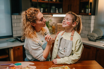 Fototapeta premium Mother painting daughter's face for easter celebration at home