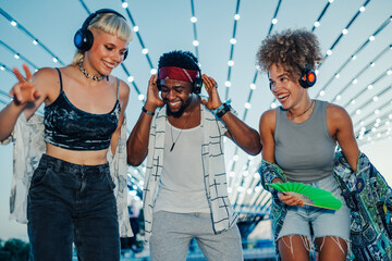 Happy friends listening to music with wireless headphones at music festival
