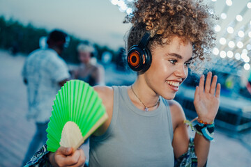 Young woman dancing at silent disco, enjoying music and cooling down with fan