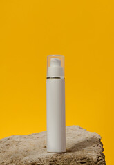 White plastic cosmetic bottle with dispenser and transparent cap on yellow background. Packaging for cream, fluid and gel