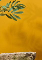 Stone on yellow background with shadow and green branch, stage for cosmetics and products demonstration