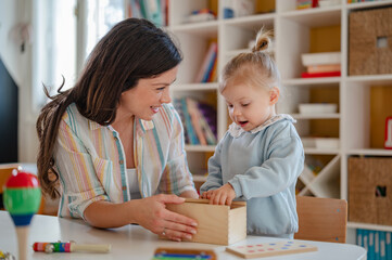 Fototapeta premium A young woman and a little girl work together on a wooden educational toy, engaging in hands-on learning activities that promote cognitive development and creativity in a bright classroom