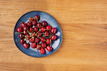 Fresh cherries on a blue plate over wooden background
