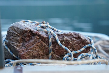 Homemade anchor made of stone, a massive stone wrapped with a blue and white rope close-up