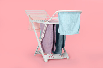 Drying rack with fresh clean laundry on light pink background