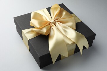 Gift box with golden bow on light grey background, closeup