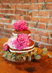 Three-tiered cake adorned with pink peonies and eucalyptus on a rustic wooden table