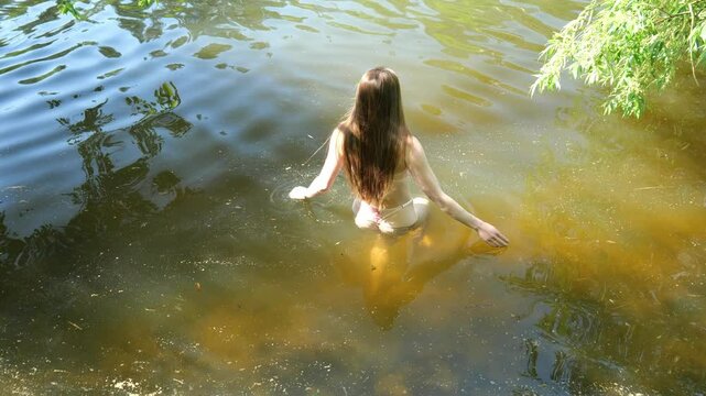 Young woman in lingerie swims in cold dirty water. Slow motion erotic portrait woman. Woman naked posing standing in water