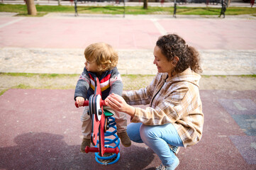 Smiling Woman Playing with Toddler on Playground Equipment on a Sunny Day