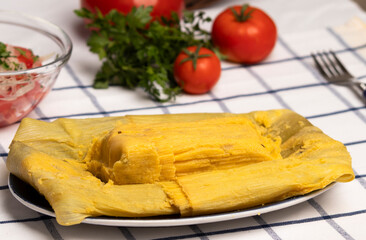 Humitas en hojas junto a tomates maduros y hojas verdes de perejil