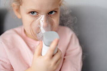 Portrait of blond child in inhalation mask with portable inhalation device with eyes close-up and steam. Childhood lung health.