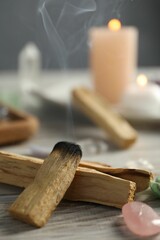 Smoldering palo santo stick and gemstone on wooden table, closeup