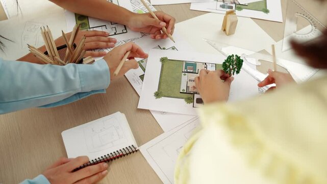 Architect and engineer use tree model discuss about building blueprint on table with architectural document, measurement tools and wooden block scatter around at modern office. Closeup. Delineation.