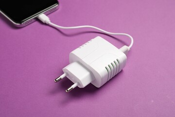 USB power adapter with charge cable connected to smartphone on purple background, closeup