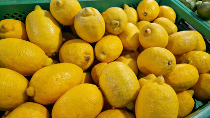 Sale of lemons in a supermarket. Citrus fruits in plastic boxes, close-up. Lemons in a store. Ripe, juicy, bright yellow lemons. A pile of lemons for sale at the market