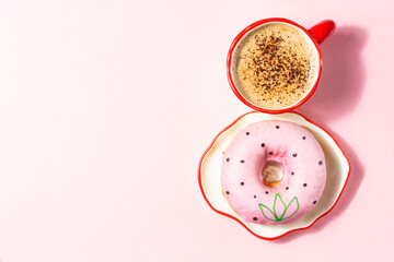 A pink donut with a floral design and a red coffee cup on a pink background. A delicate and festive composition for International Women's Day.