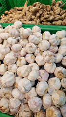 Garlic close up in supermarket. Lots of garlic in plastic green box on market stall. Garlic in green plastic box at farmers market. Garlic for sale in store. Display of fresh produce for sale