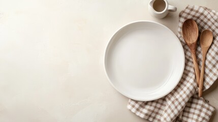 Empty white plate with wooden spoons on a checkered cloth, evoking a rustic kitchen or dining scene.