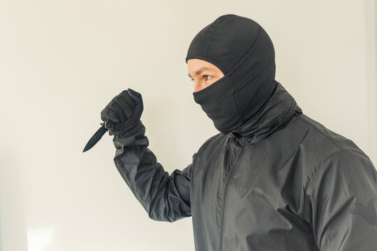 Masked Intruder: Holding a Knife
A person dressed in black tactical gear and a balaclava, gripping a knife in a threatening stance. - Powered by Adobe
